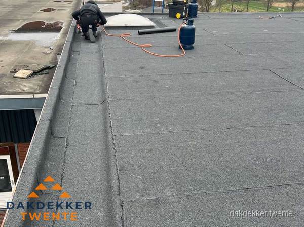 Dakdekker repareert bitumen dakbedekking op groot plat dak in Twente