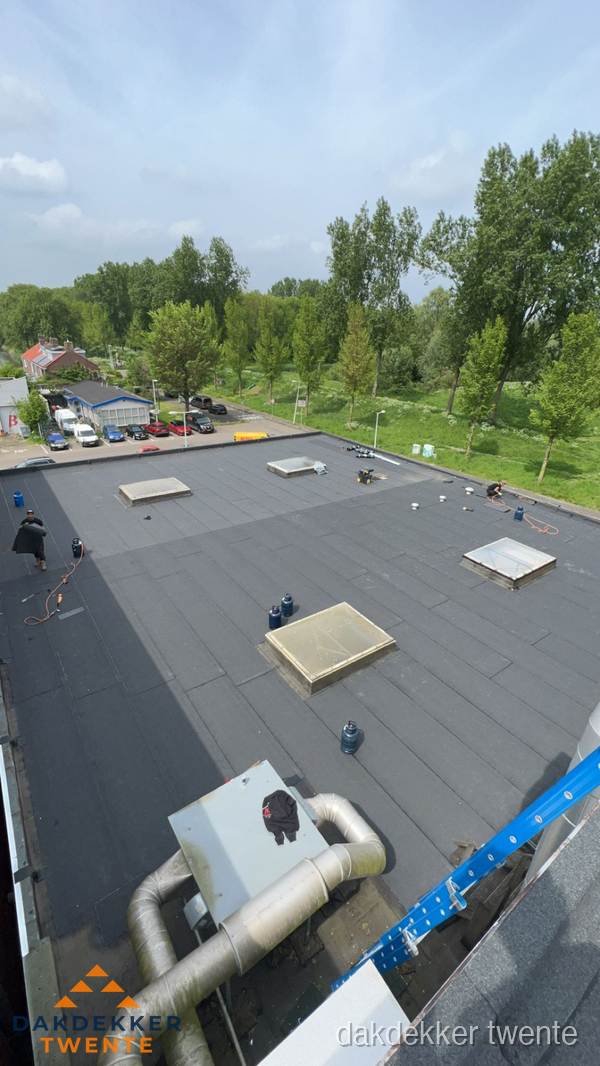Dakdekker aan het werk op groot plat dak met bitumen in Twente